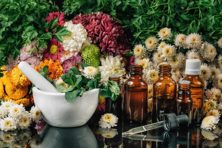 Mortier avec des herbes, flacons en verre et fleurs colorées en arrière-plan.